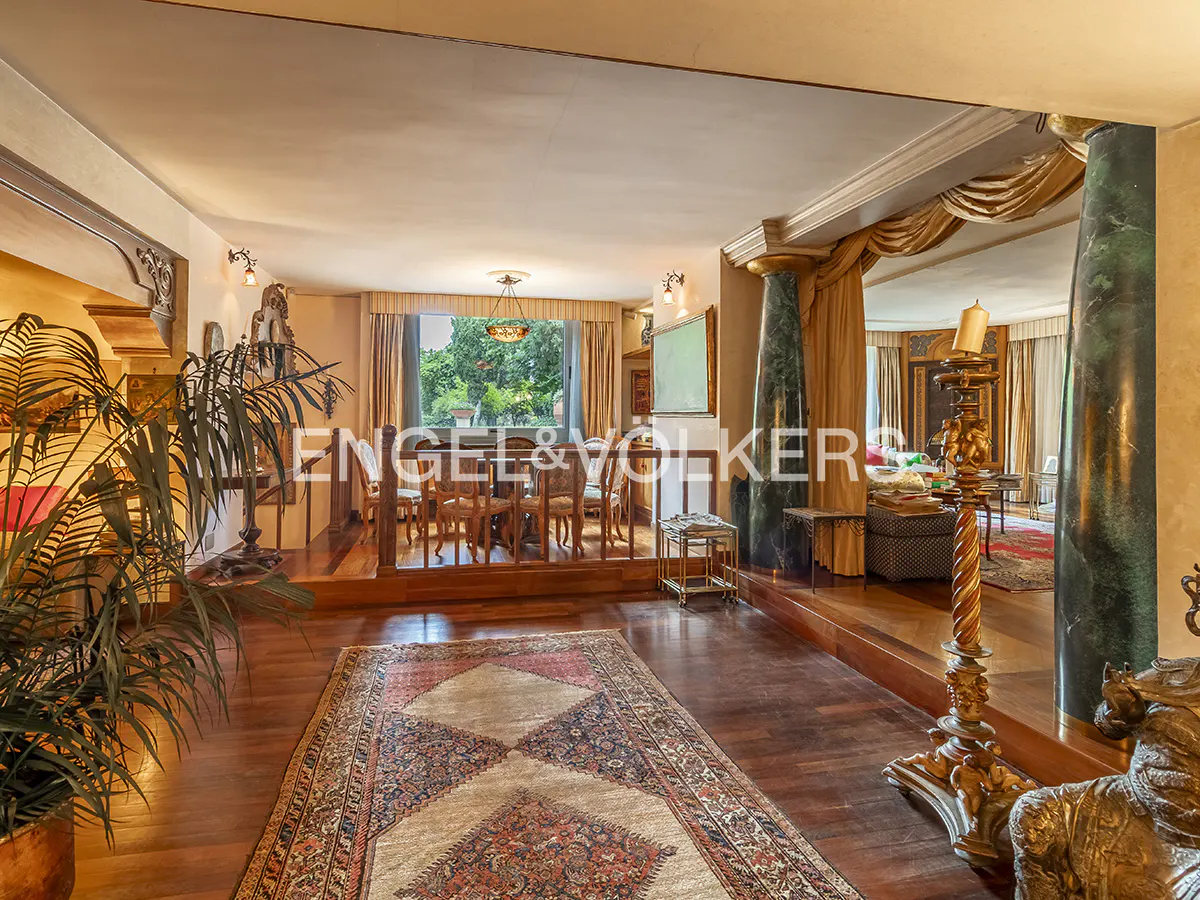 Elegant living room with hardwood floors, a patterned rug, green marble columns, and a raised dining area with garden views.