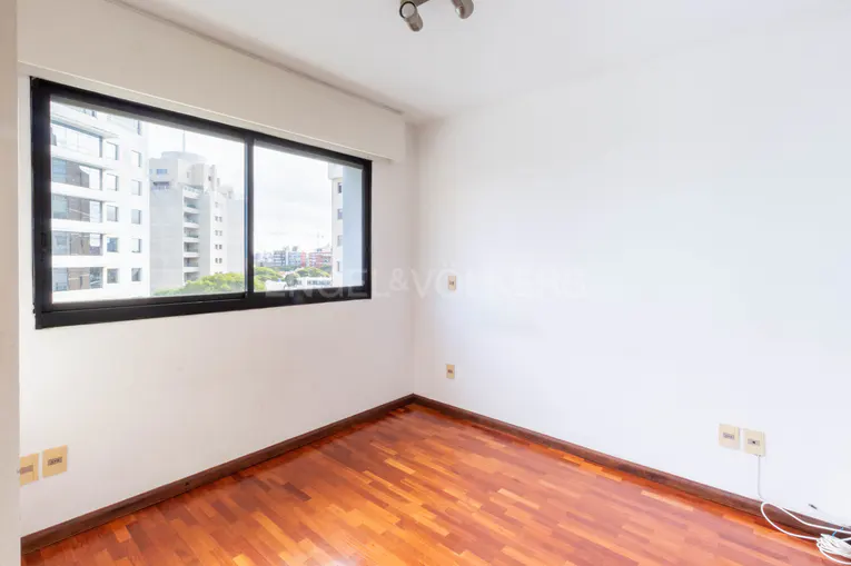 Empty room with wood floors, white walls, and a black-framed window showing a city view.