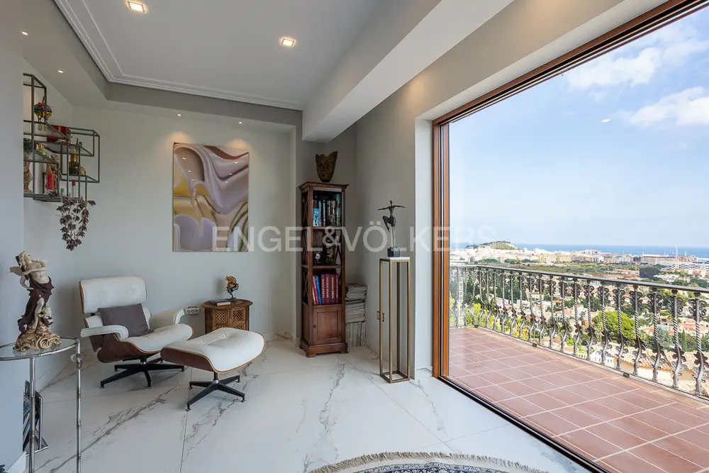 Bright living room with white marble floors, a white chair, and a balcony overlooking a city and the ocean.