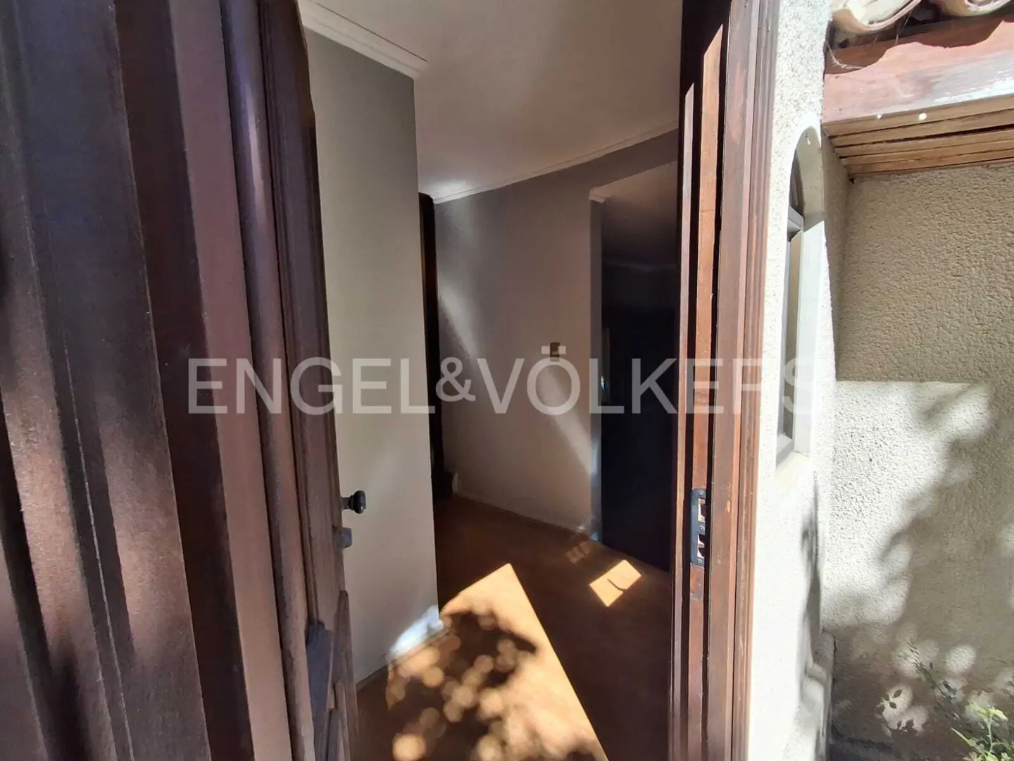 A partially open wooden door reveals a hallway with light brown floors and gray walls. The Engel & Völkers logo is visible on the door.