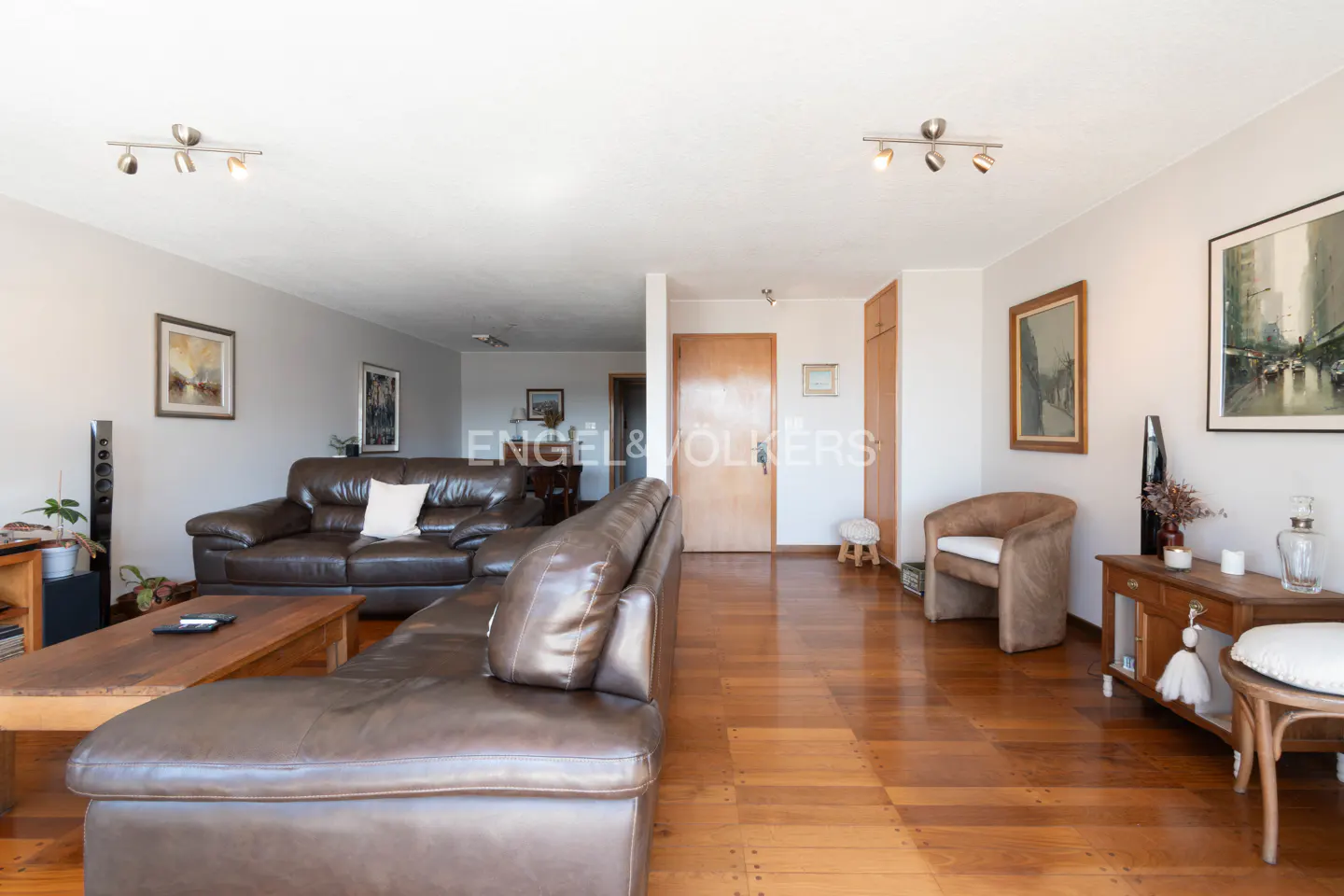 Living room with brown leather sofas, wood floors, and neutral walls. Artwork and furniture add to the inviting space.