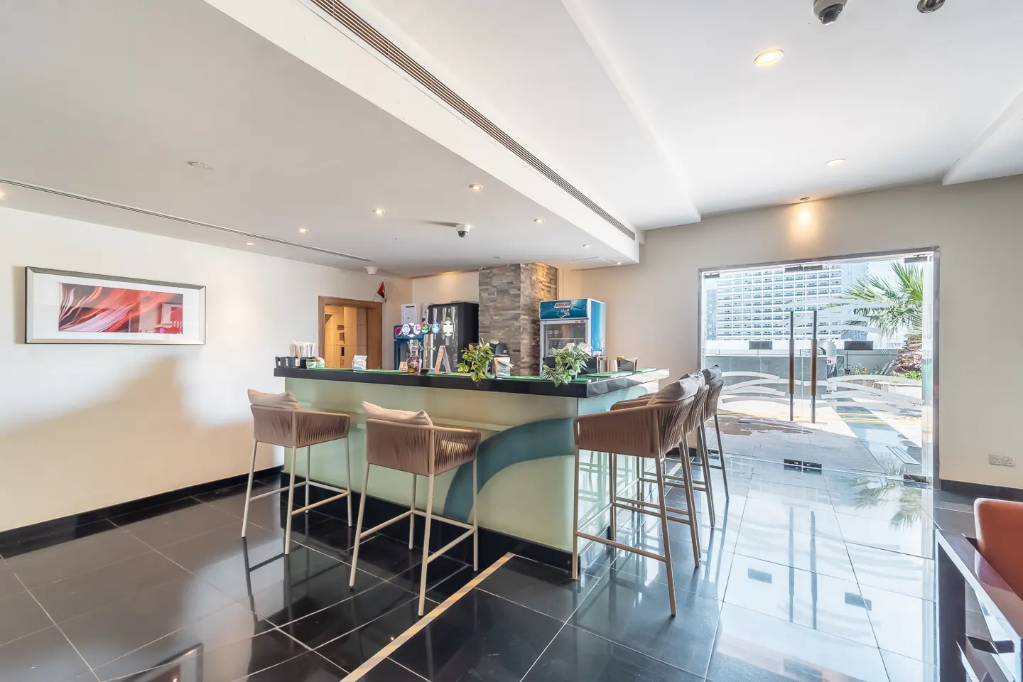 Indoor bar area with black tile floor, bar with stools, drink fridges, and glass doors to an outdoor patio.