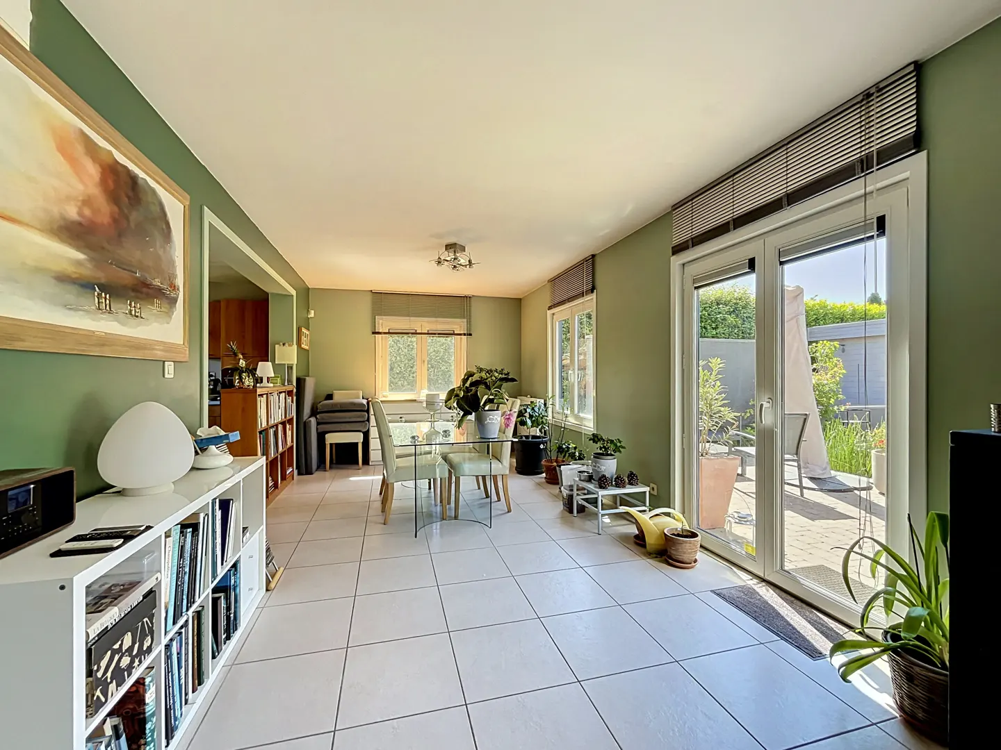 A bright, green-walled dining room with a glass table, white tile floors, and a sliding glass door to a patio.