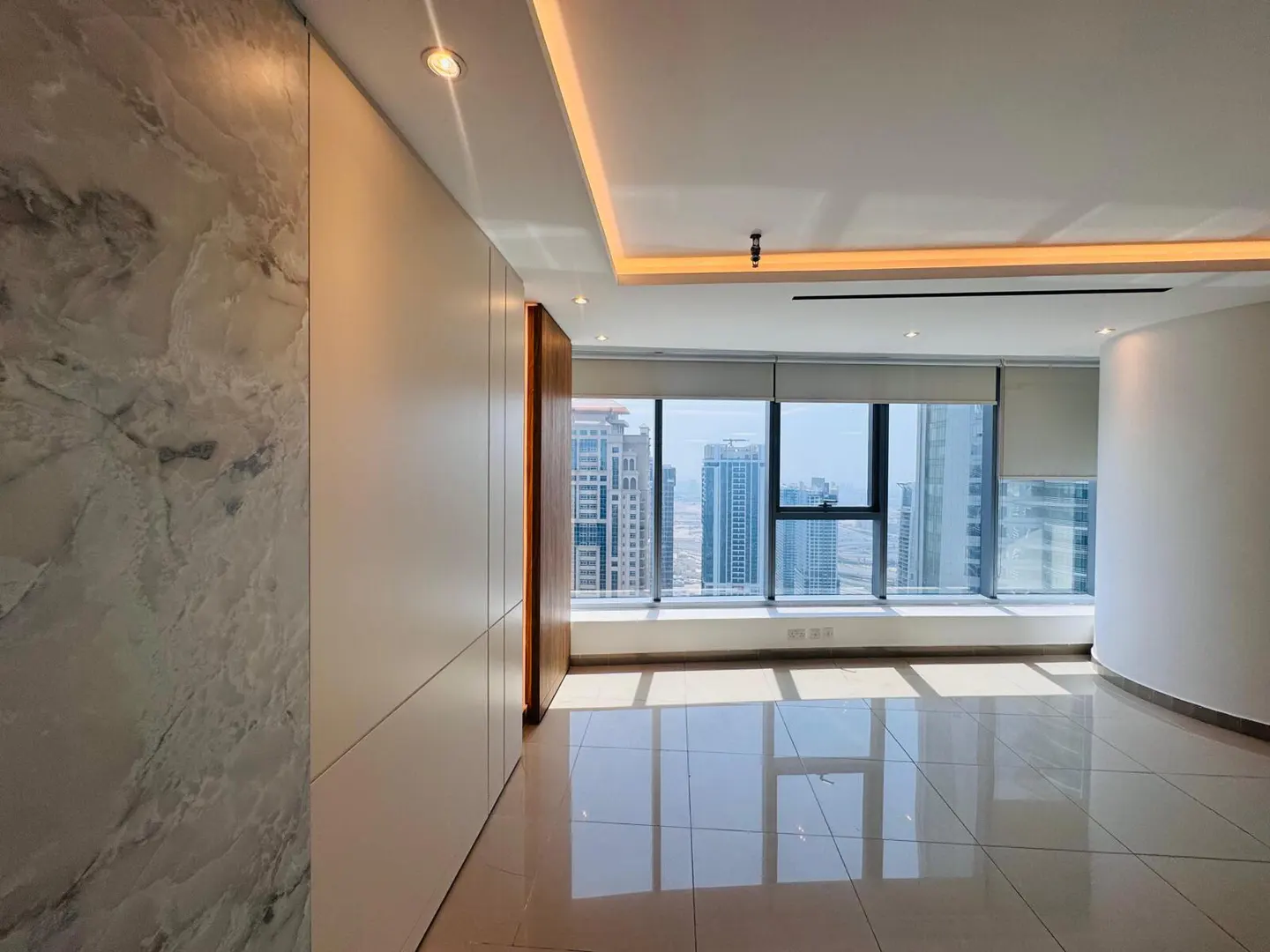 Bright, empty room with tile floors and a large window overlooking a city skyline. Marble accent wall on the left.