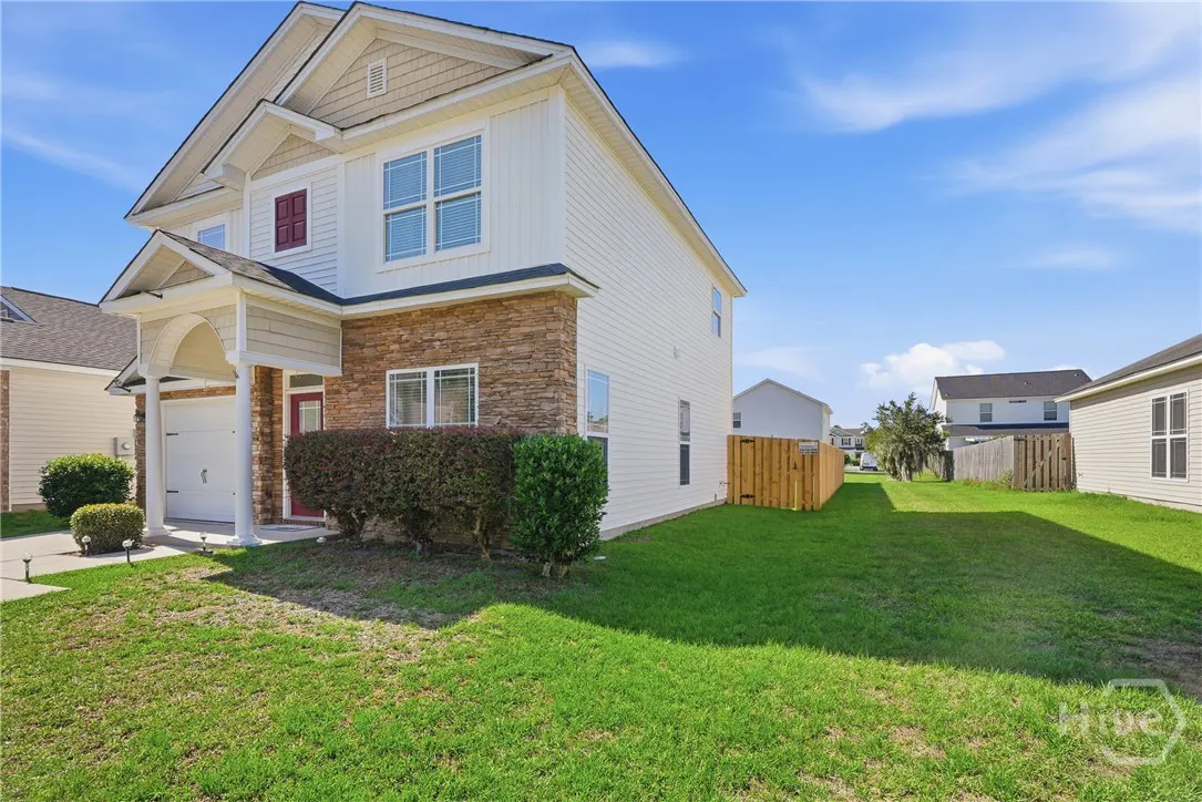 Two-story house with white siding, stone accents, red door, and green lawn under a blue sky.