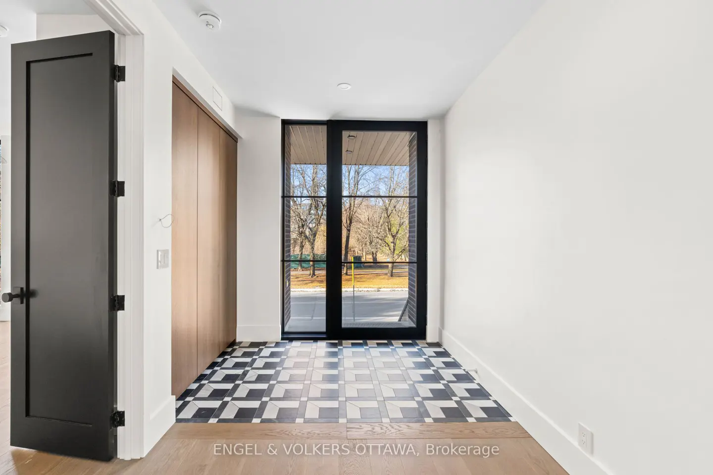 Entryway with black door, wood closet, and black-framed glass door to outside. Black and white patterned tile floor.