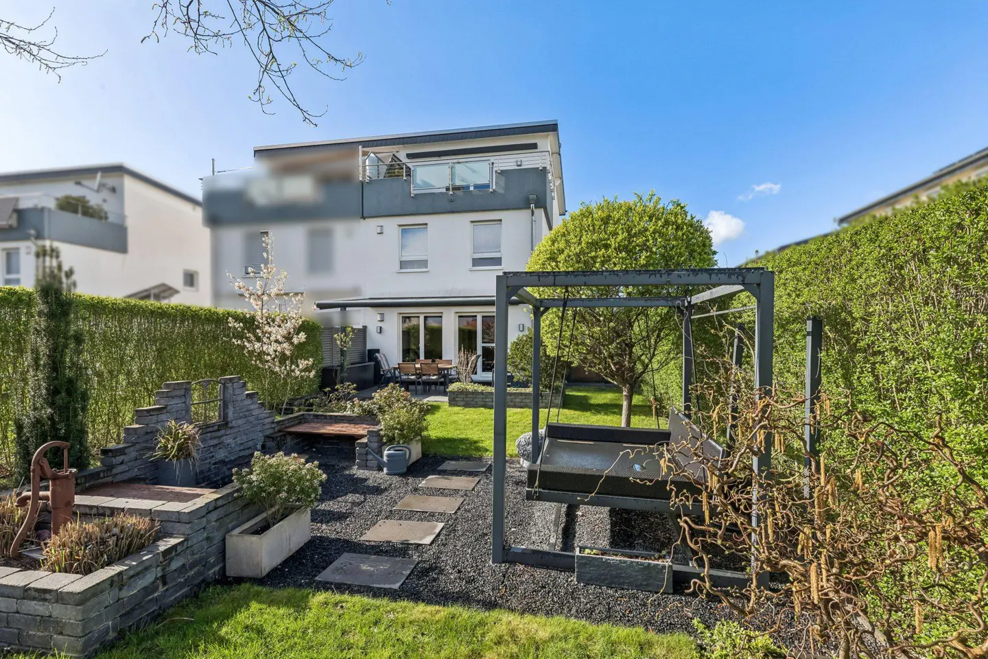Backyard of a modern white house with a green lawn, stone path, and a metal swing set.