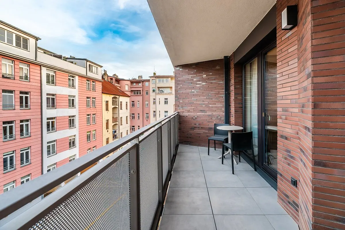 Modern balcony with a small table and two chairs, overlooking a city street with colorful apartment buildings.