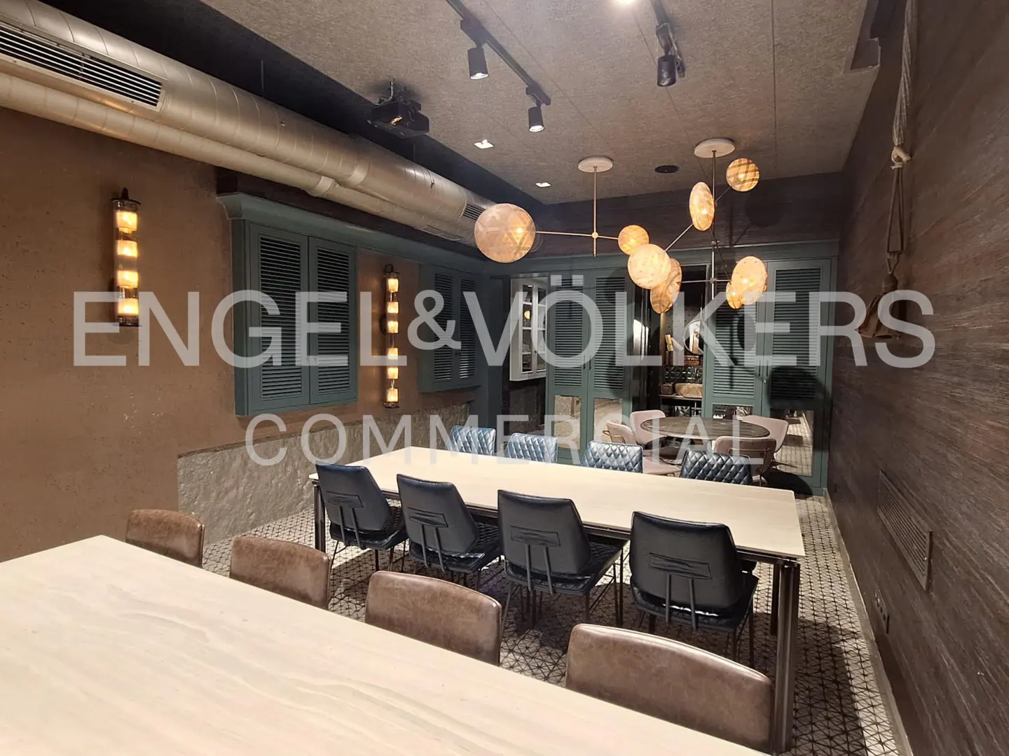A modern office space with long tables, blue chairs, and globe pendant lights. Shutters on the windows and textured walls add character.