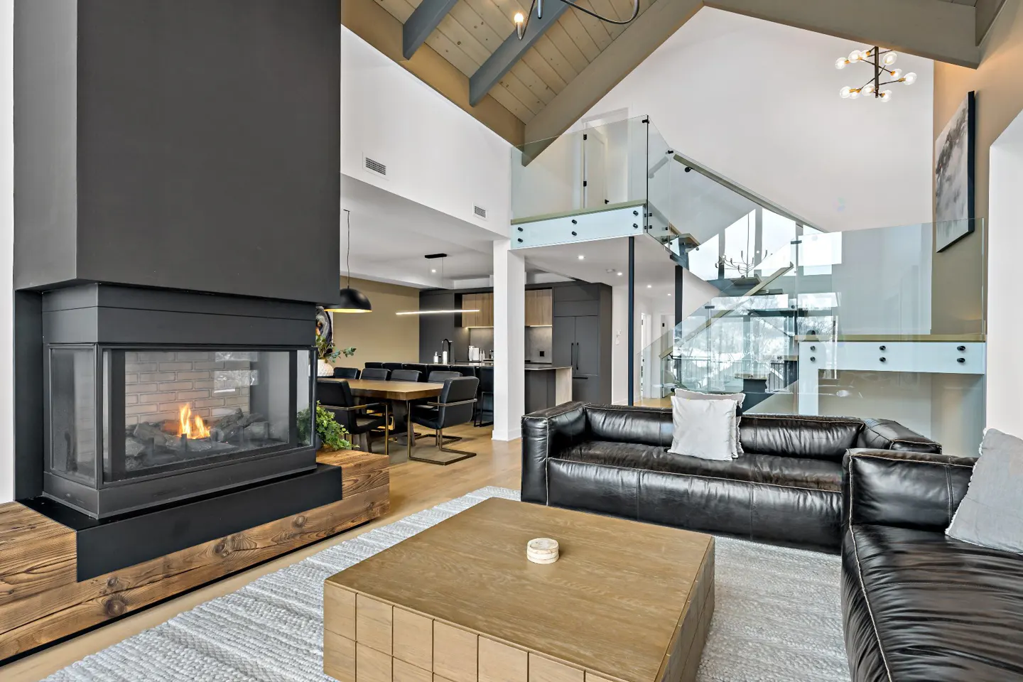 A modern living room with a black fireplace, leather sofas, and a glass staircase.