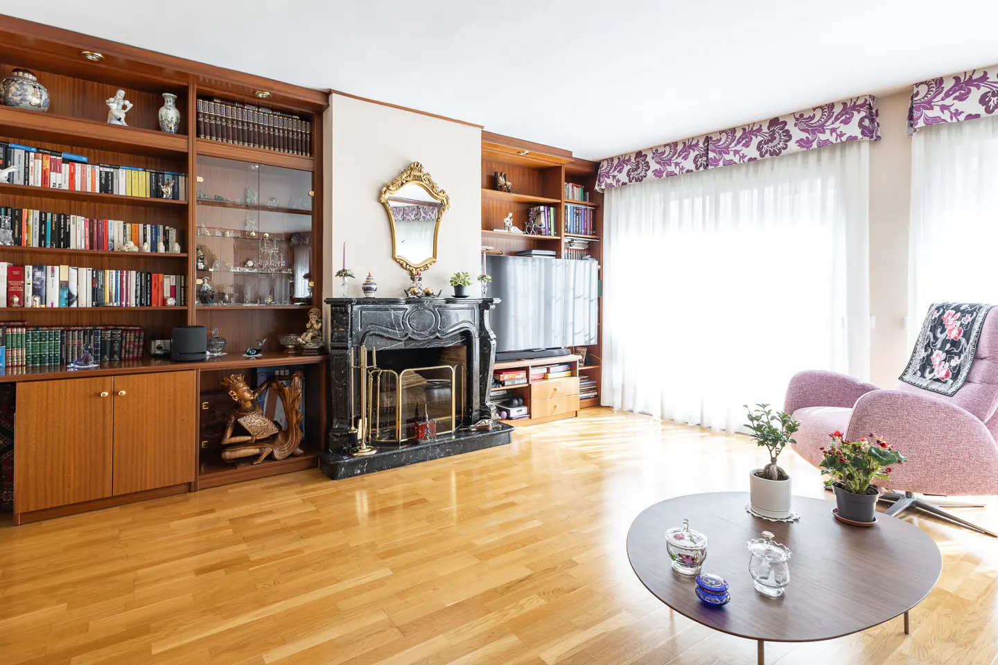 Living room with wood floors, built-in bookshelves, black marble fireplace, and a round coffee table with glass jars.