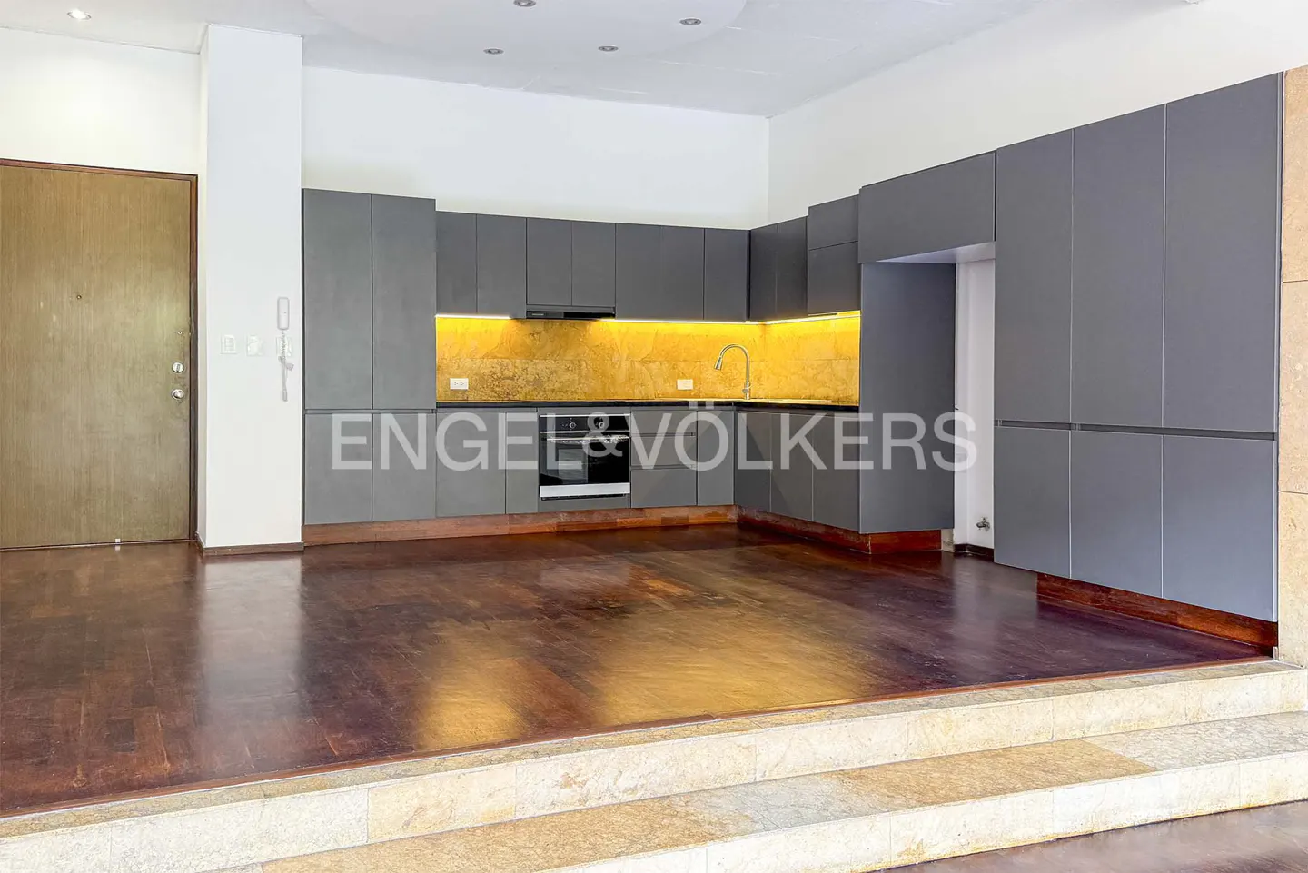 Interior view of a modern kitchen with gray cabinets, wood floors, and stone steps leading up to the kitchen area.