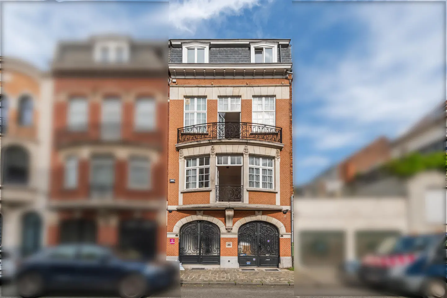 A narrow, four-story brick building with black iron gates and balconies under a blue sky.