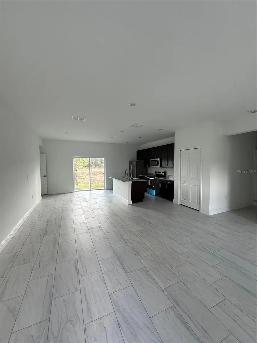 Open-concept living space with gray tile floors, white walls, and dark kitchen cabinets. Sliding glass doors lead to the outside.