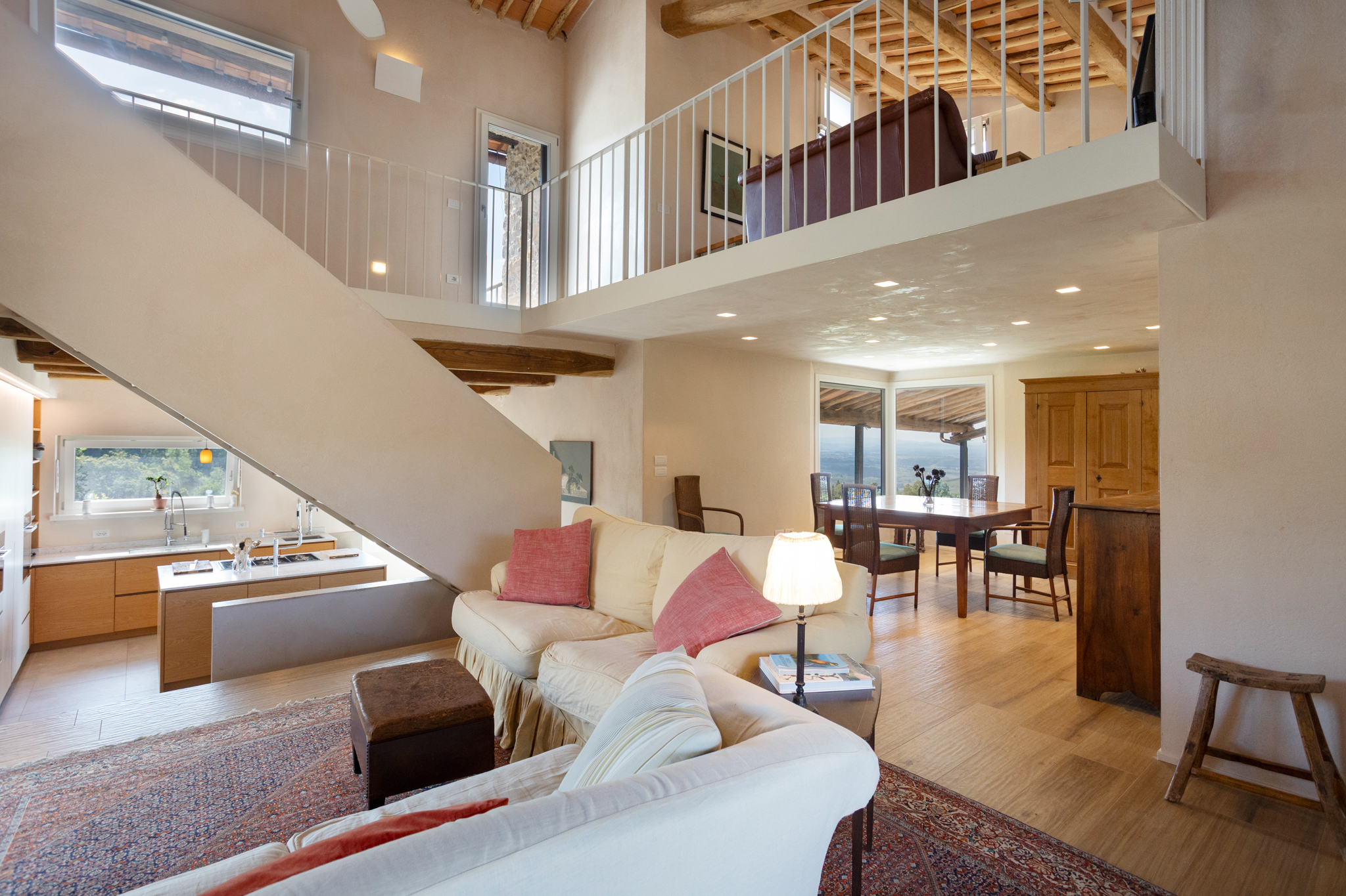 Open-plan living area with a cream sofa, dining table, modern kitchen, and a mezzanine level with a white railing. [AI-generated text]