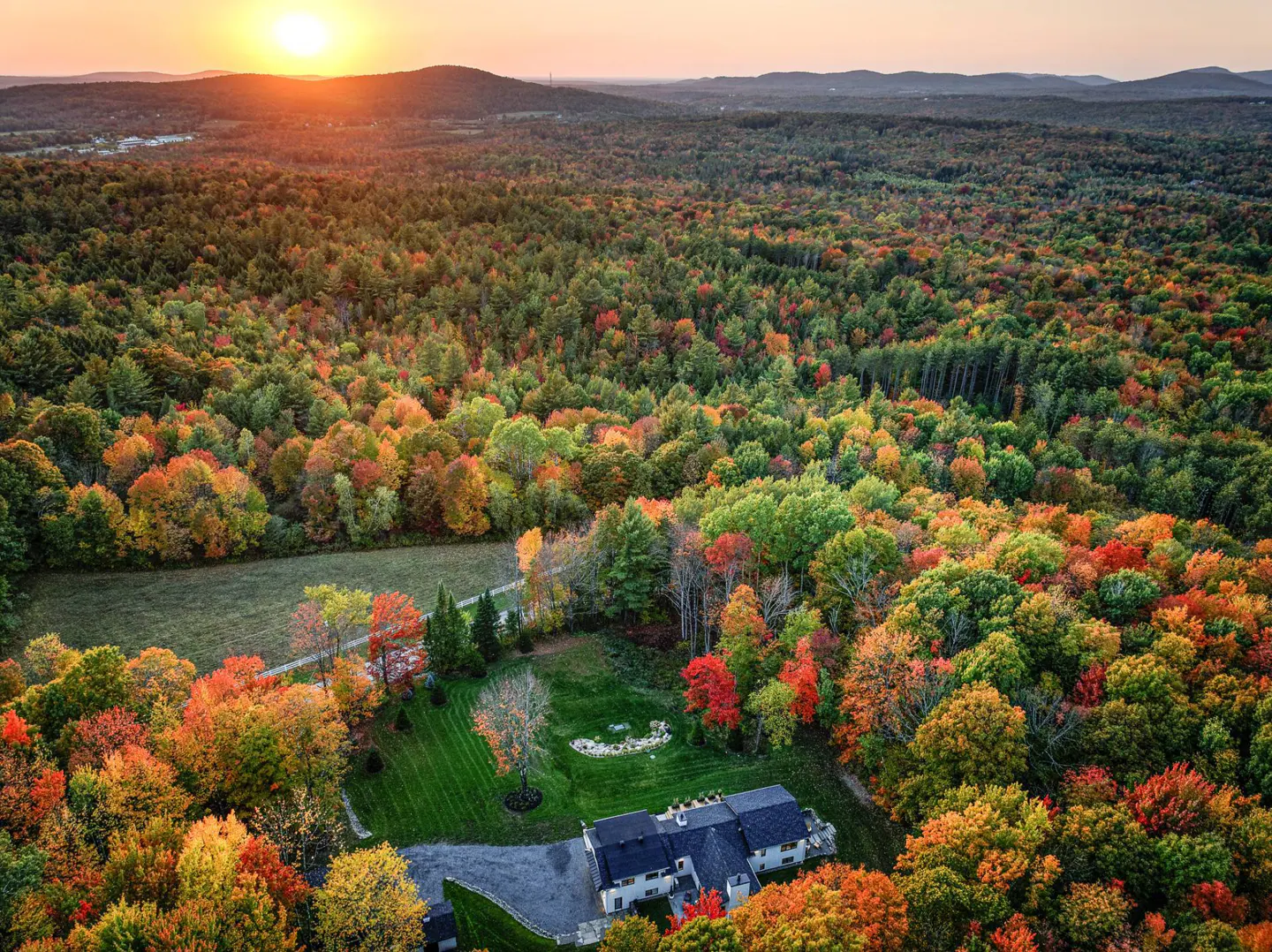 Aerial view of a house surrounded by colorful fall foliage at sunset.