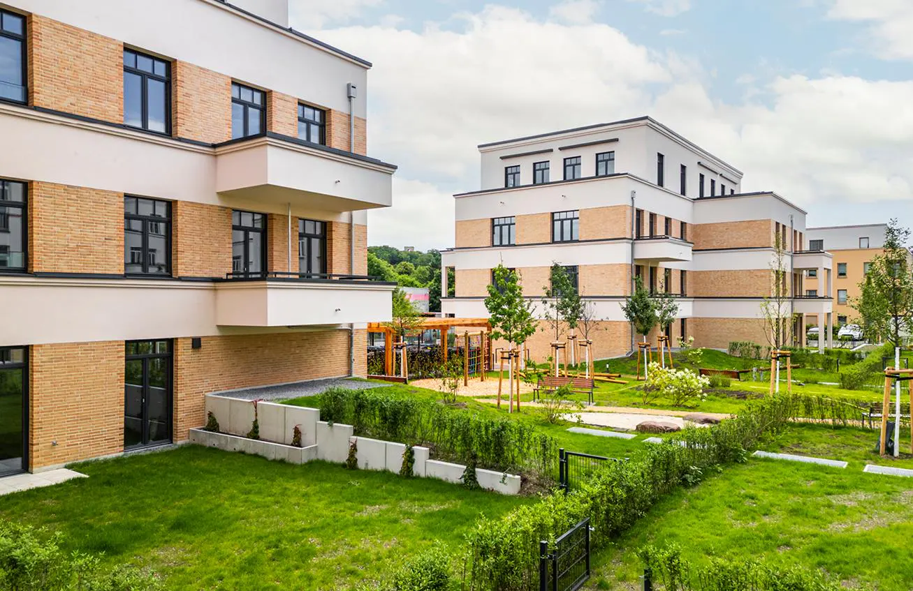 Modern apartment buildings with brick and white facade, black windows, and green lawn and garden in the foreground.