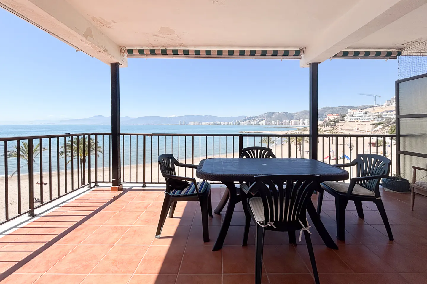 Balcony with black table and chairs overlooking a beach and ocean view.