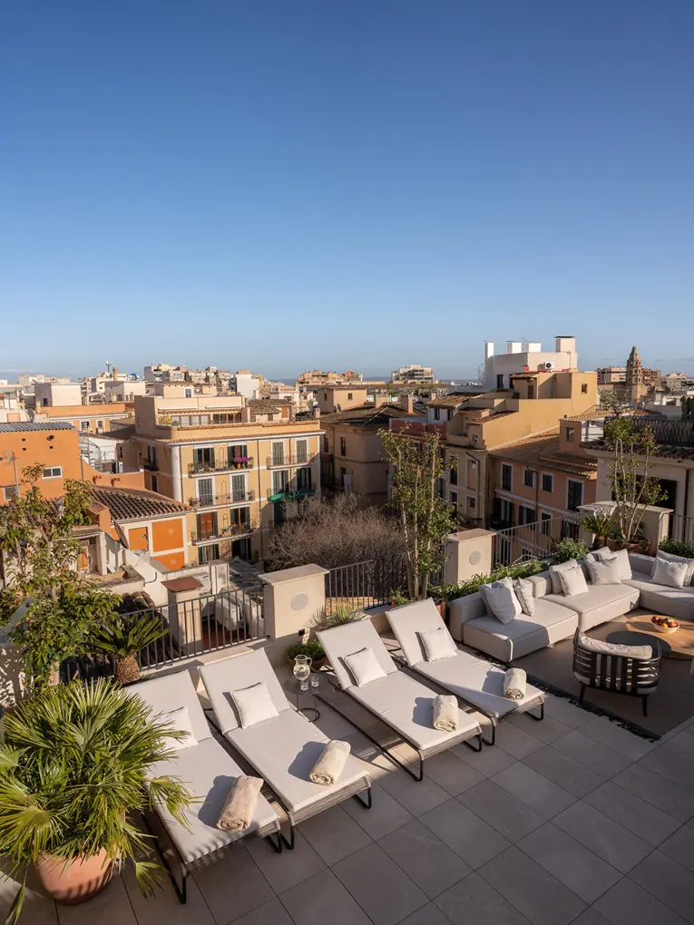 Rooftop patio with lounge chairs, sofa, and city view. Blue sky.