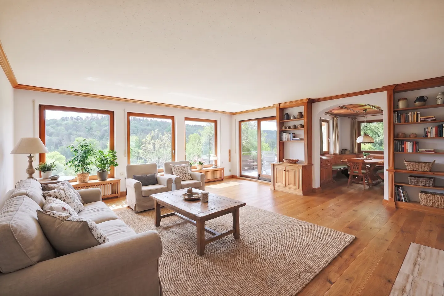 Bright living room with hardwood floors, beige sofa, two armchairs, wooden coffee table, and built-in bookshelves.