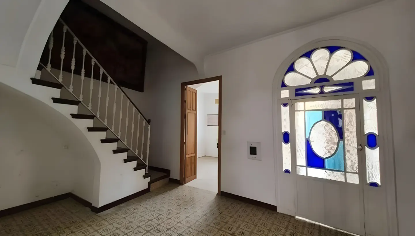 Interior view of a home's foyer with a staircase, open doorway, and a stained-glass window with blue accents.