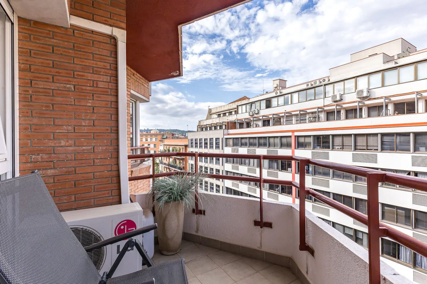 A balcony with a red brick wall, a gray chair, and a view of a city with white buildings.
