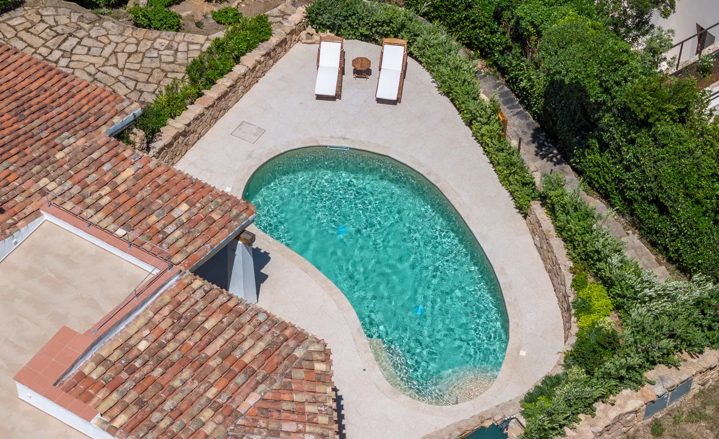 Aerial view of a kidney-shaped pool with turquoise water, two lounge chairs, and a red-tiled roof.