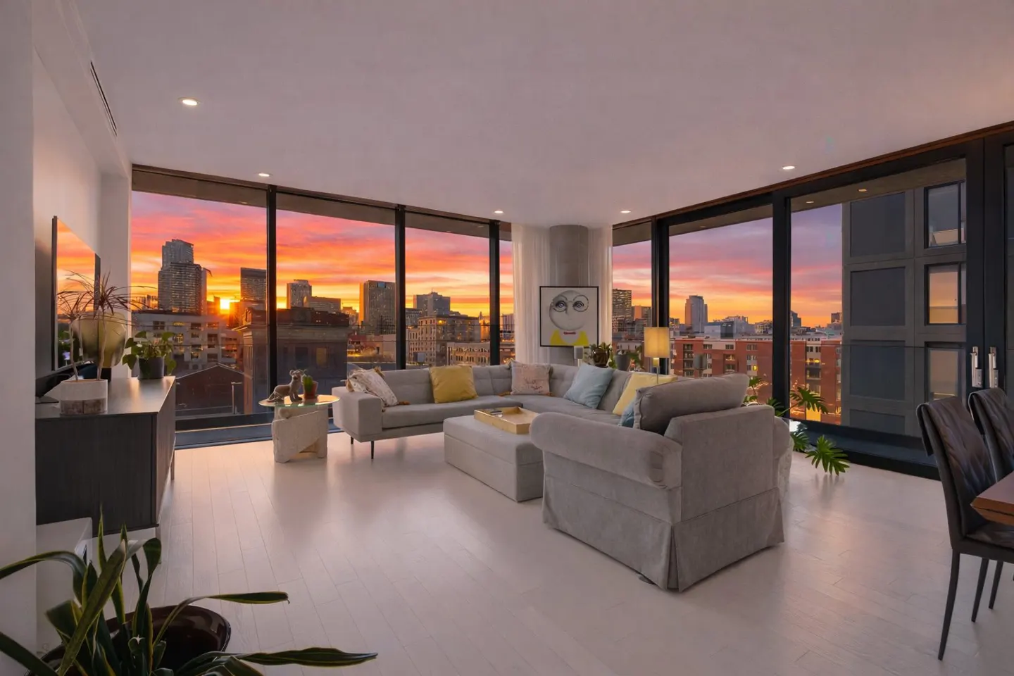 Living room with a gray sectional sofa, white floors, and a sunset view through large windows.
