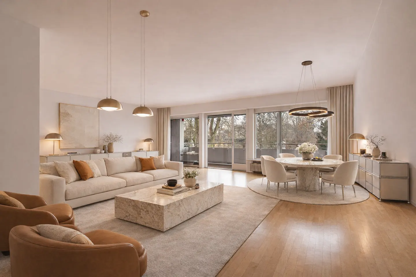 Open-concept living and dining area with a beige sofa, marble table, and round dining table with six chairs. Large windows overlook trees.