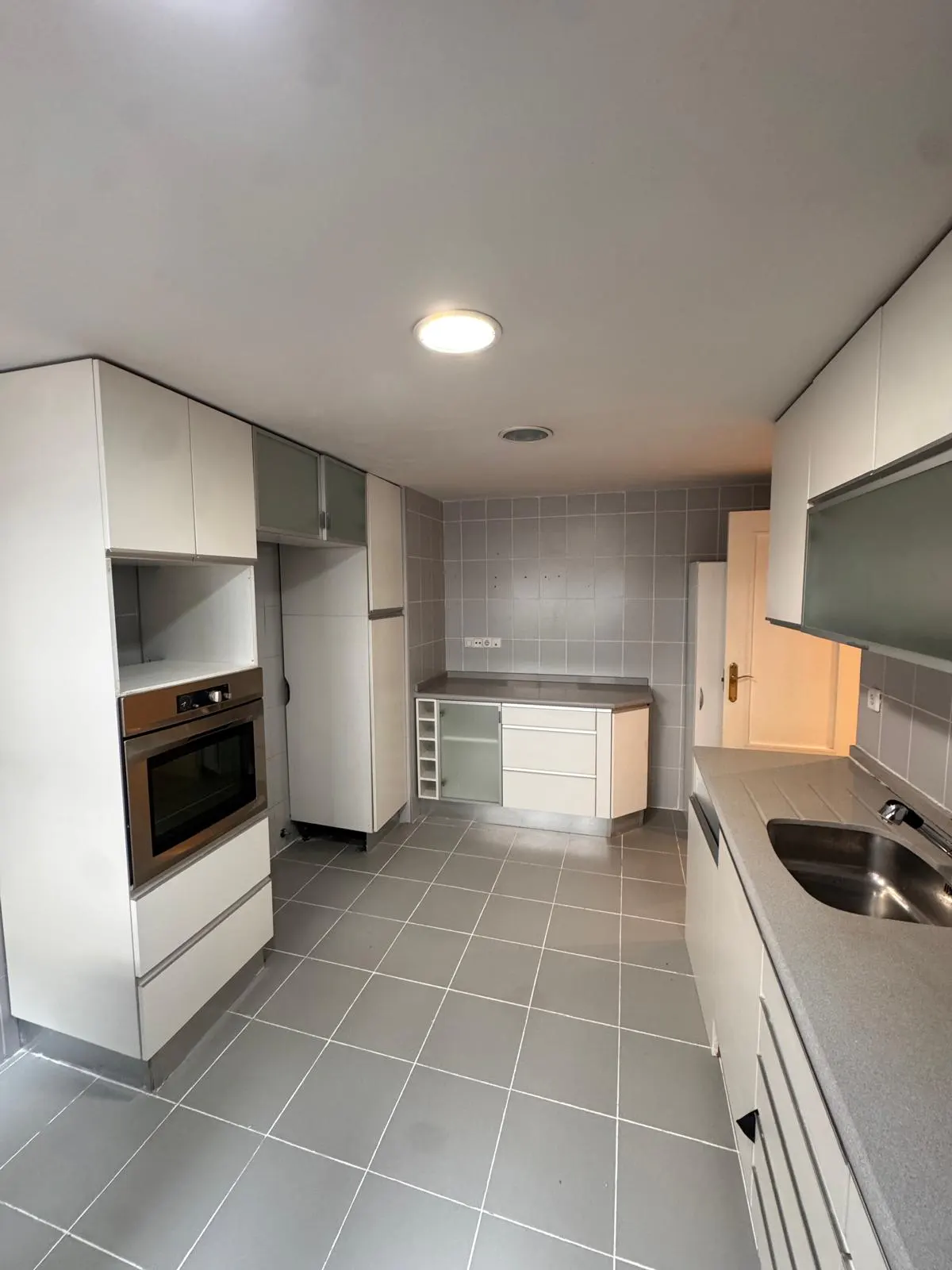A bright kitchen with white cabinets, stainless steel oven, gray countertops, and gray tiled floor.
