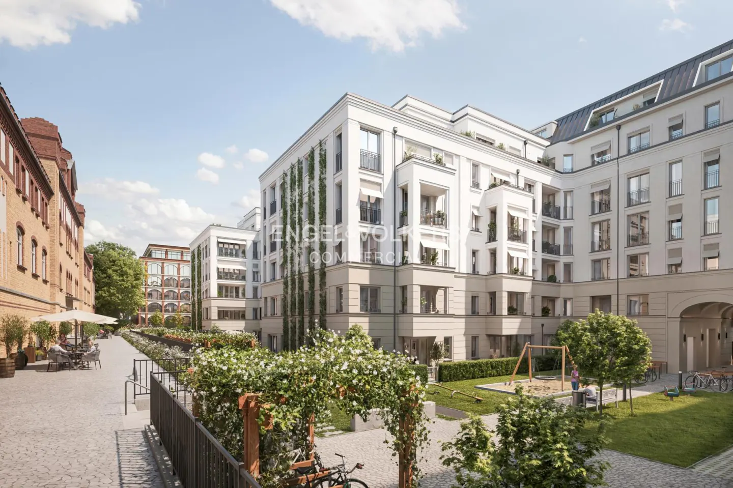 Modern white apartment buildings with climbing vines, a courtyard with a playground, and a paved walkway with outdoor seating.