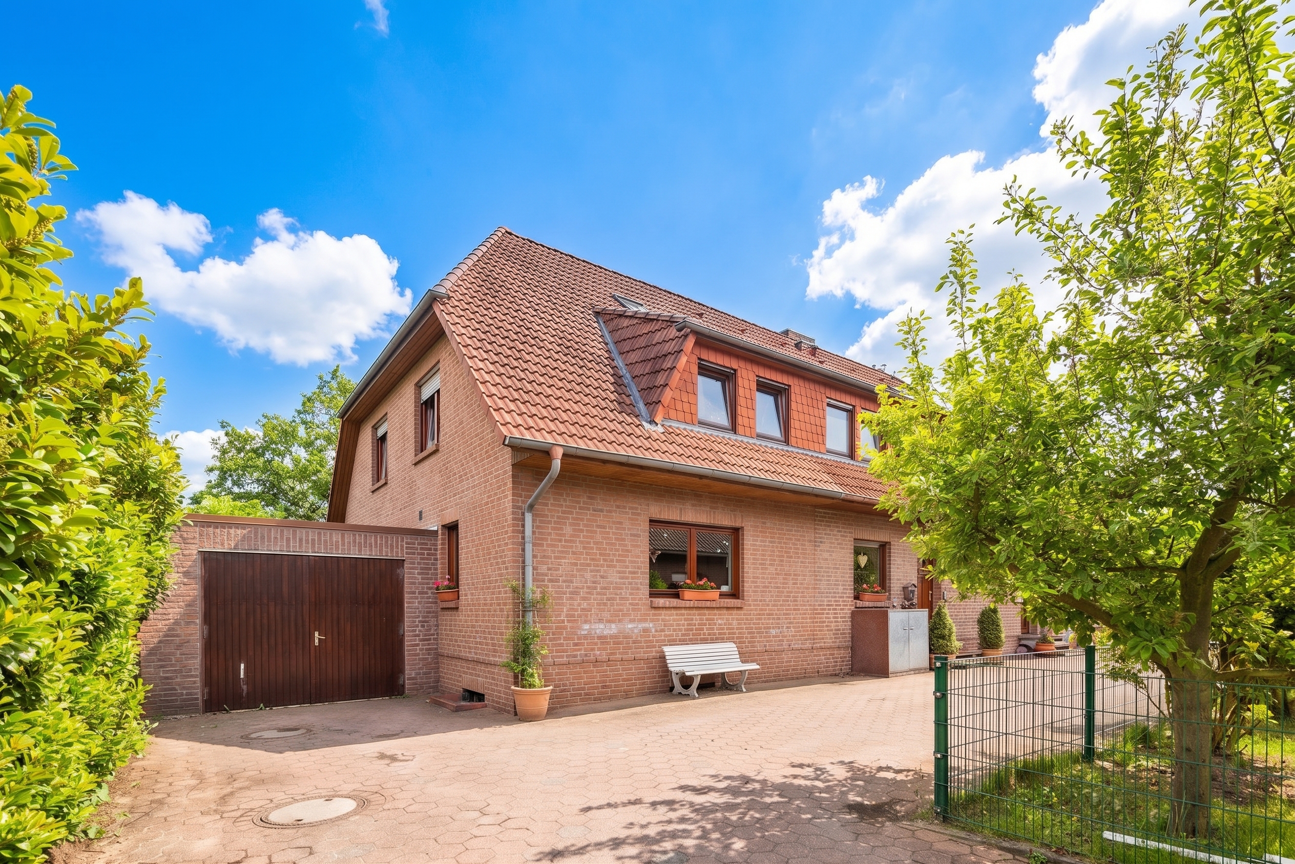 A two-story red brick house with a tiled roof, attached garage, white bench, and a green tree under a blue sky. [AI-generated text] [AI-modified]