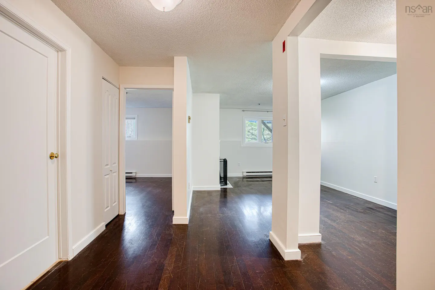 Hallway with dark wood floors, white walls, and doorways leading to other rooms. A white door is on the left.