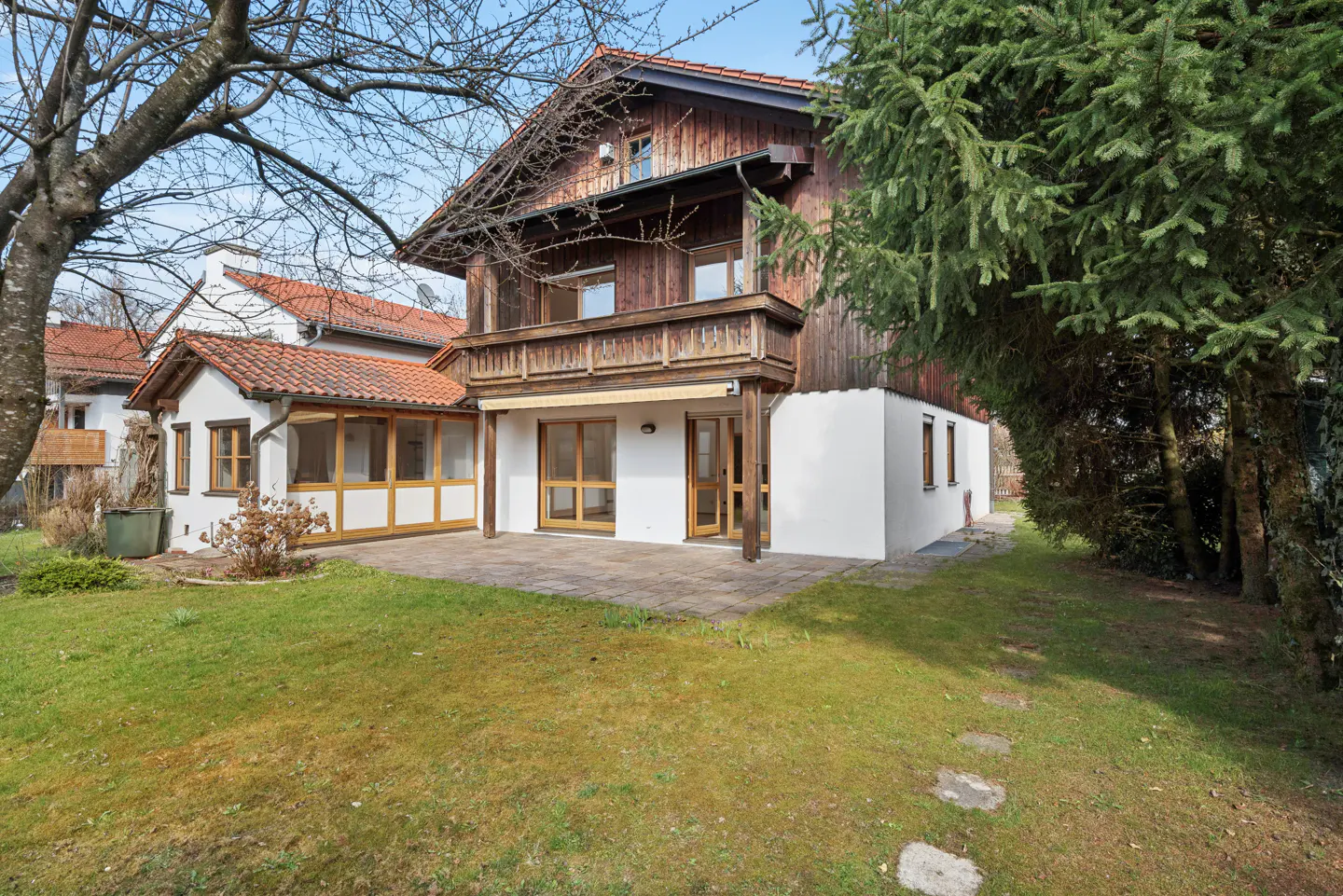 Two-story house with wood siding on the upper level and white siding on the lower level, with a balcony and a patio.