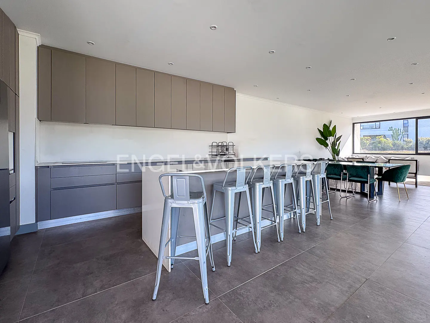 A modern kitchen with gray cabinets, a white island with silver stools, and a dining table with green chairs.