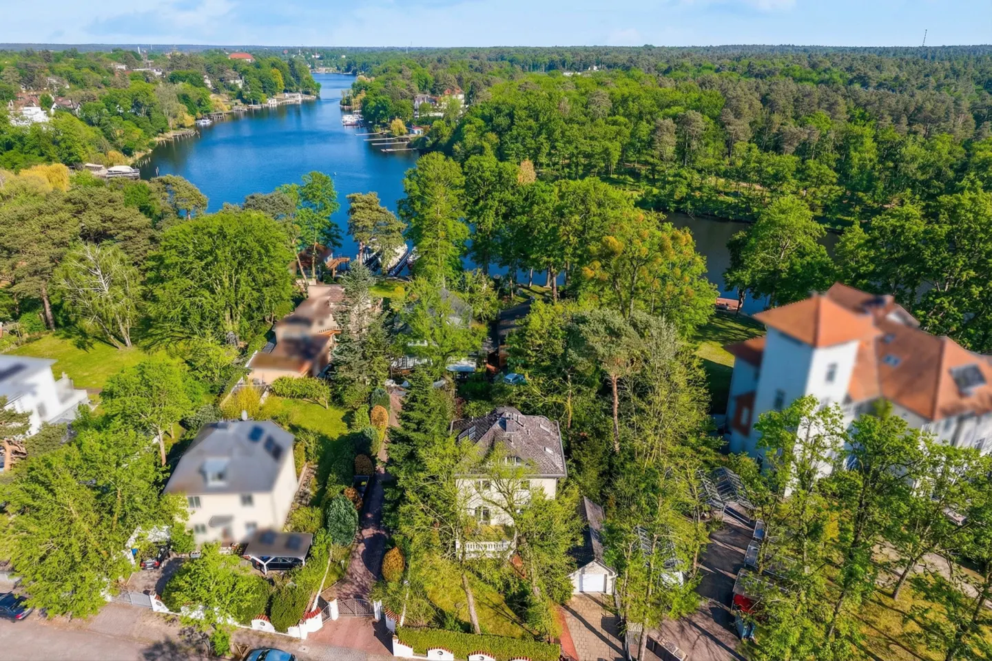 Aerial view of houses nestled among green trees near a blue lake under a bright sky.