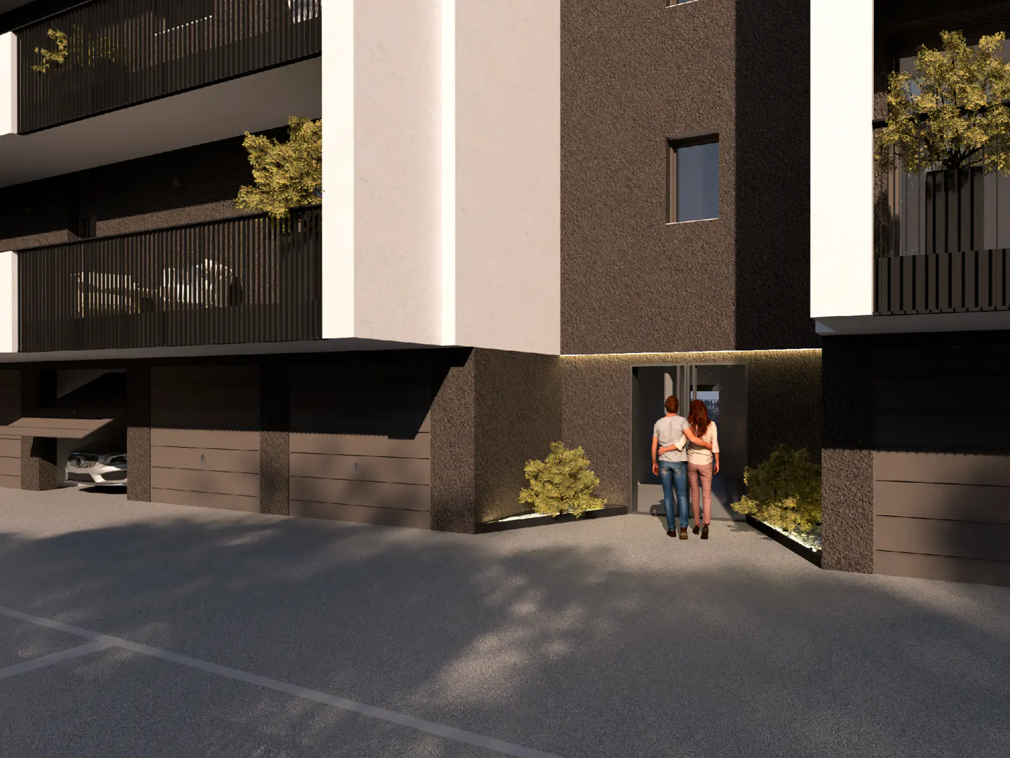 Exterior view of a modern apartment building with a couple walking towards the entrance. The building is dark gray and white with black balconies.