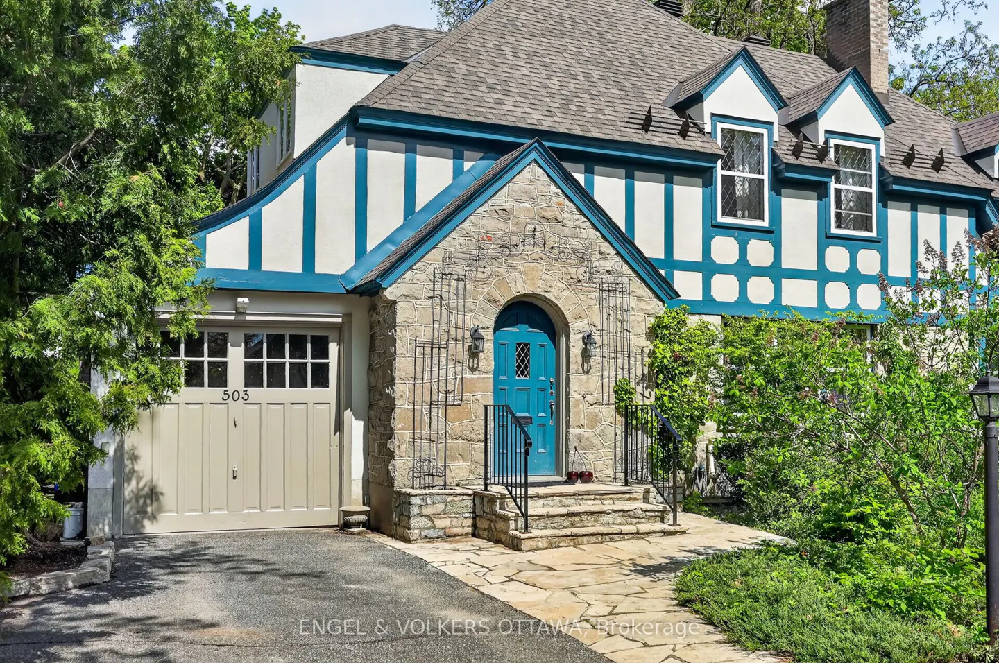 Exterior of a Tudor-style house with a blue door, stone facade, and a beige garage door with the number 503.
