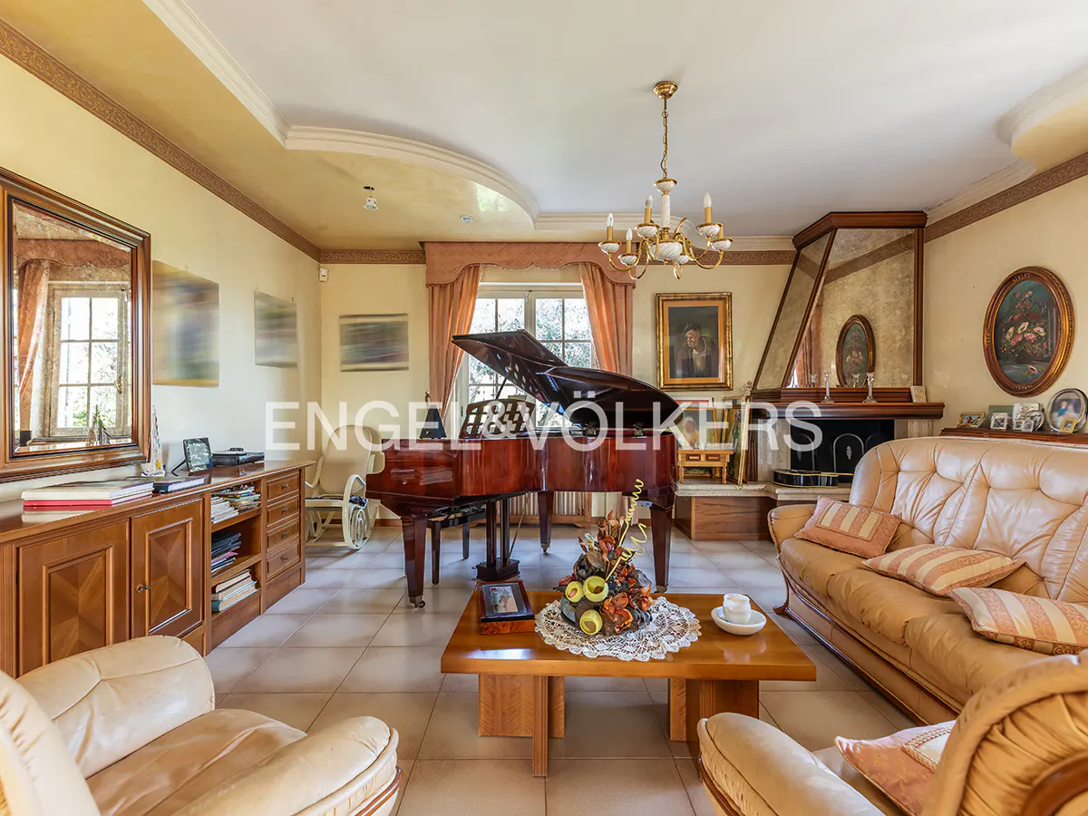 Living room with a grand piano, tan leather sofas, and a fireplace. A chandelier hangs from the ceiling.