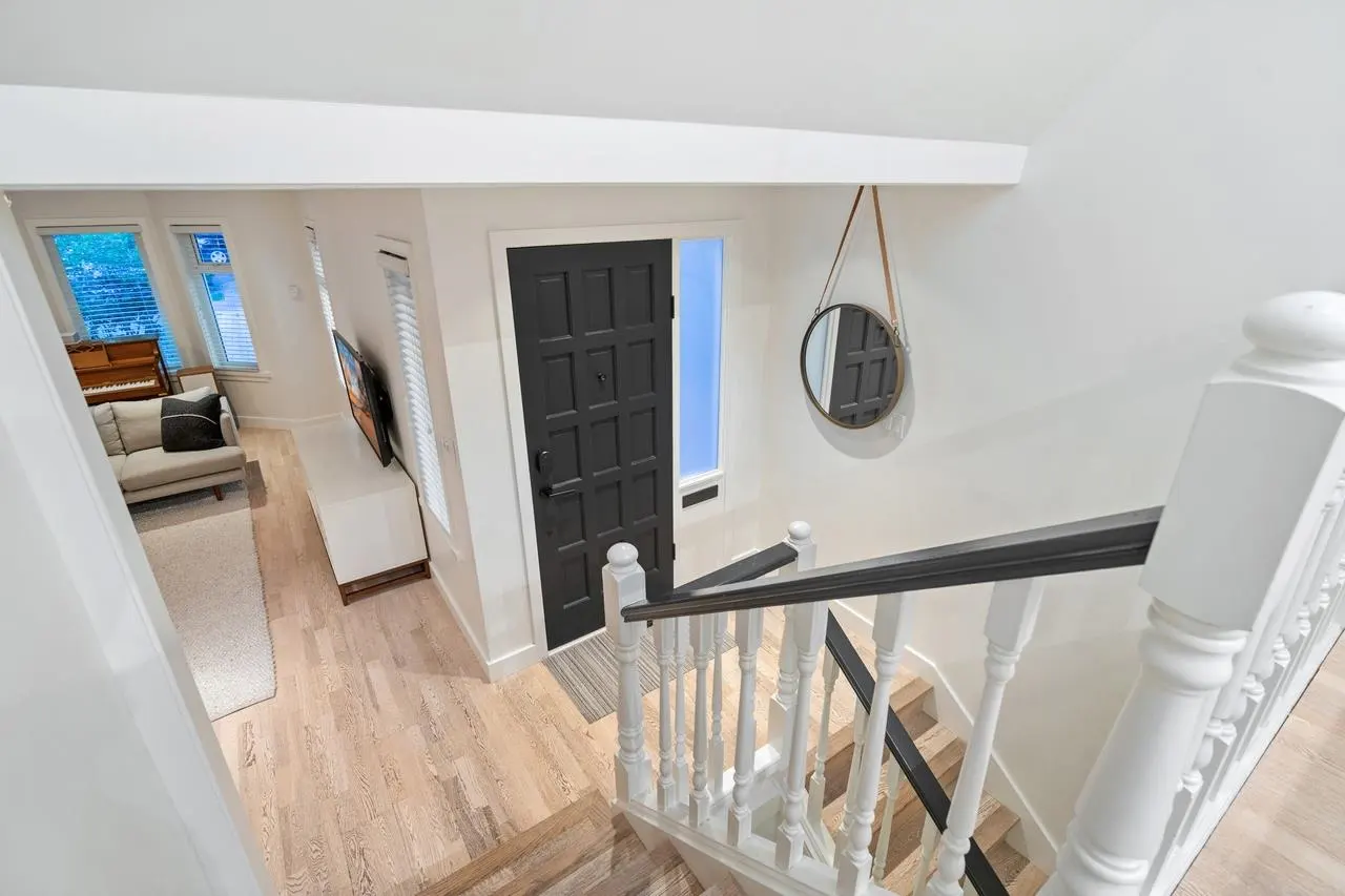 A high-angle shot of a home's interior, featuring a staircase with white railings, a black front door, and a glimpse of the living room.