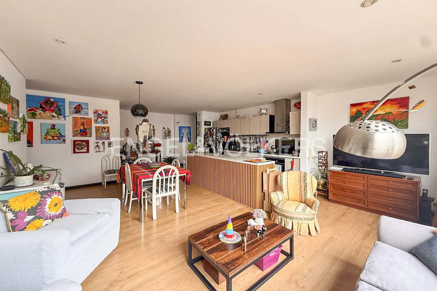 Open-concept living space with wood floors, a dining table, kitchen island, and colorful art on the walls.