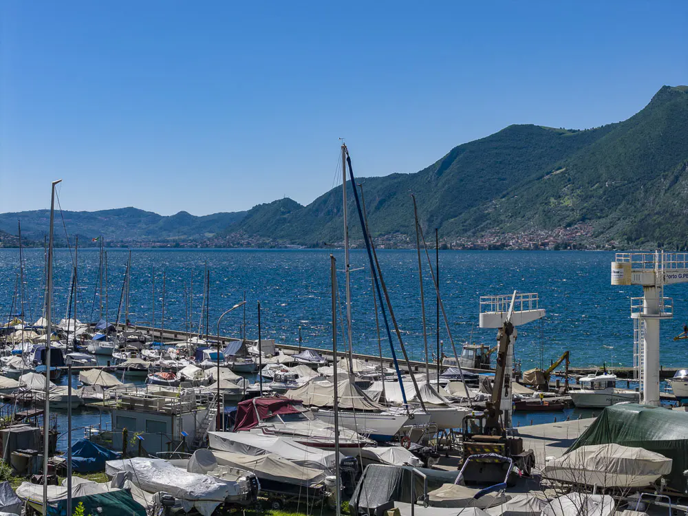 Scenic view of a marina filled with boats, covered and uncovered, on a sunny day with mountains in the background.