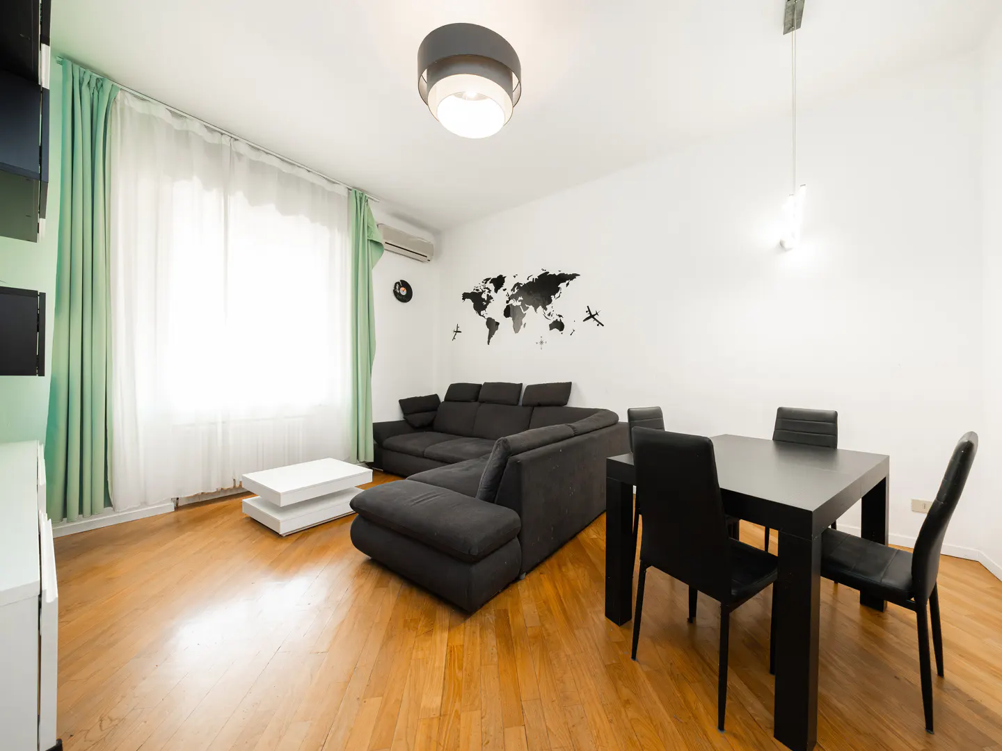 Bright living room with hardwood floors, a gray sectional sofa, a black dining table with four chairs, and a world map wall decal.
