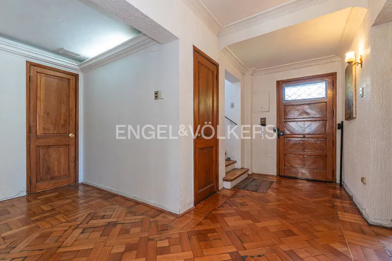 Entryway with herringbone wood floors, white walls, and two wood doors. A staircase is visible in the background.