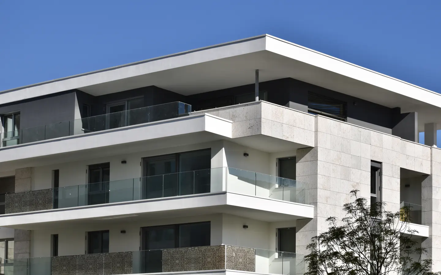 Modern apartment building with white balconies and glass railings against a clear blue sky.