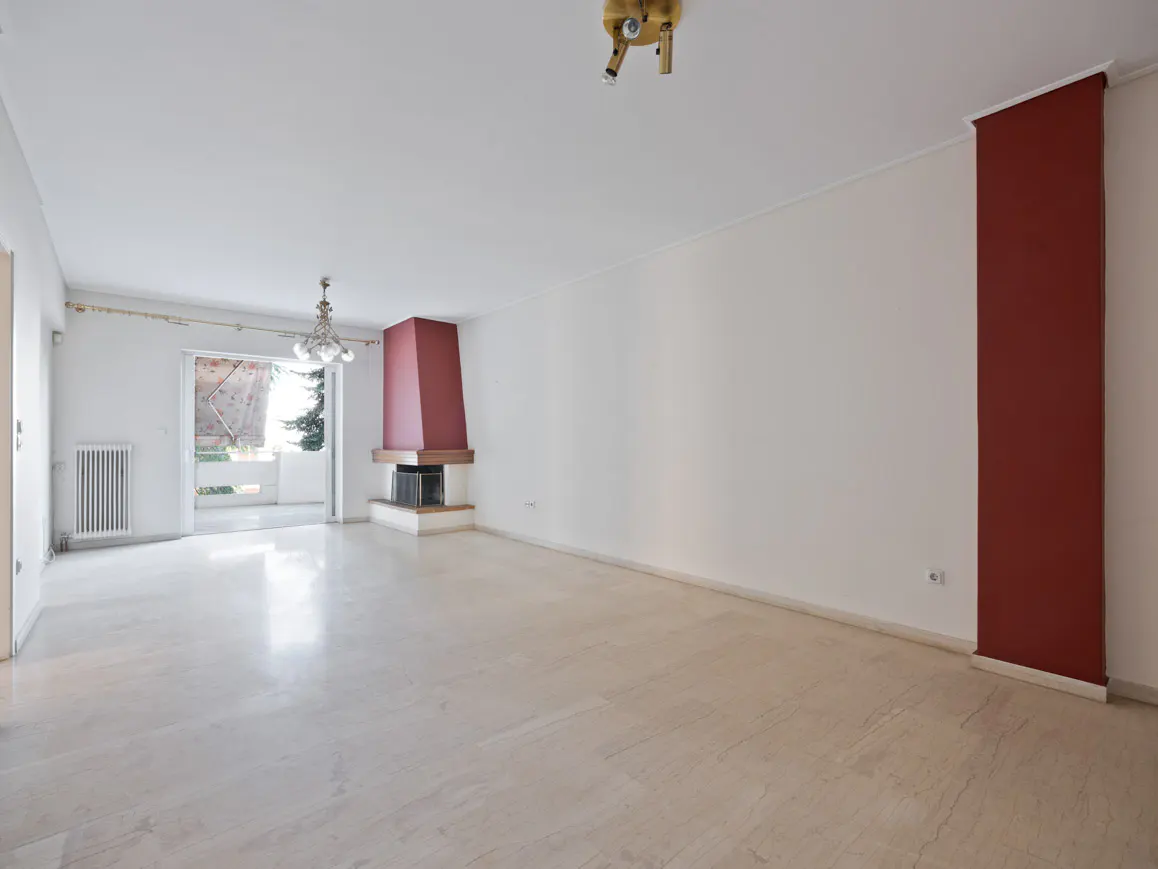 Bright, empty room with marble floors, white walls, and a red accent wall. A fireplace and balcony are visible.
