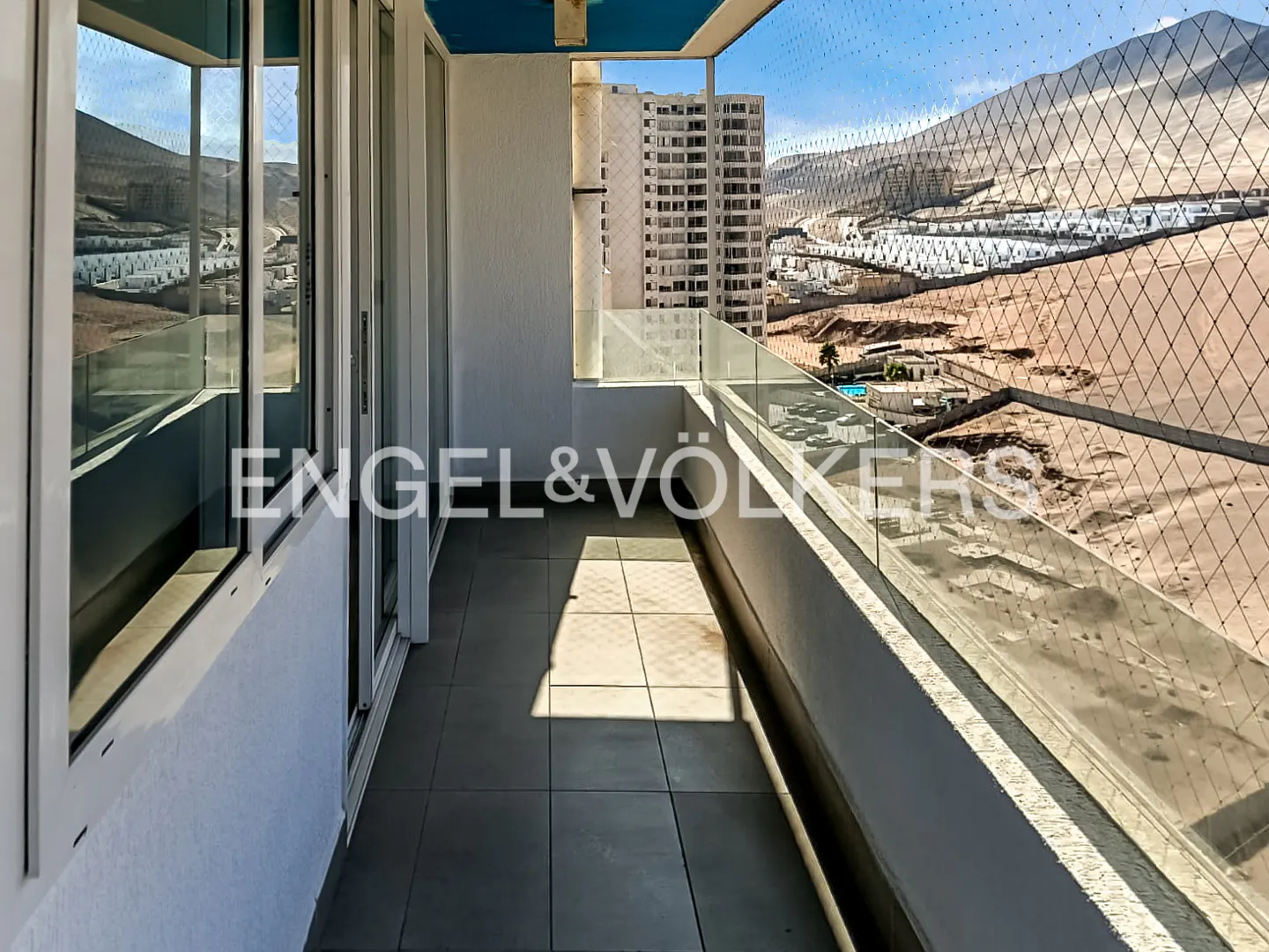 Balcony view with Engel & Völkers logo. Gray tile floor, glass railing, and a view of buildings and a mountain.