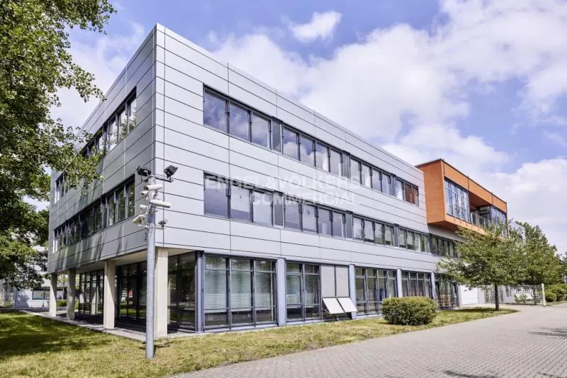 Modern, three-story commercial building with gray metal siding and large windows under a partly cloudy sky.