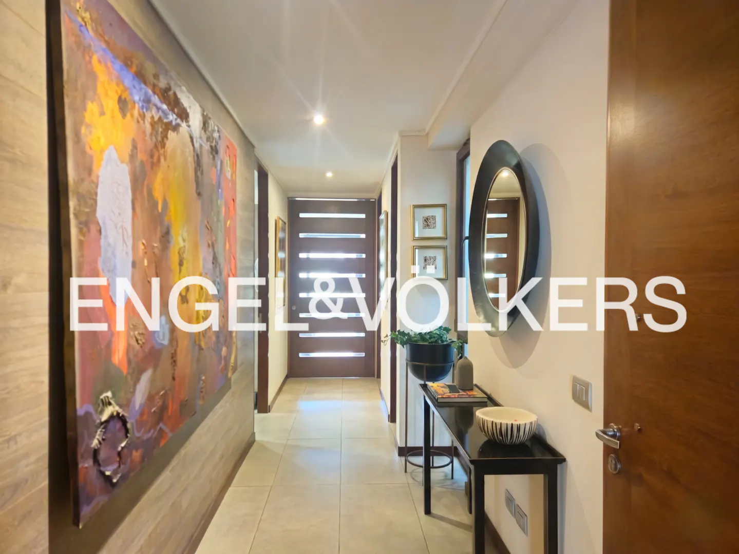 A modern hallway with a large abstract painting, a dark wood door, and a black console table with a mirror.