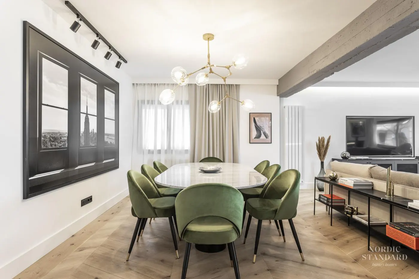 Bright dining room with a white marble table surrounded by green velvet chairs. A black and white cityscape art piece hangs on the wall.